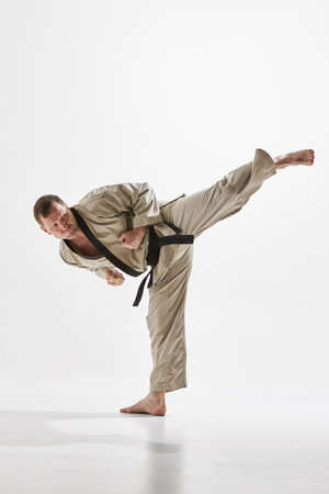 Skilled man, focused taekwondo athlete executing powerful side kick, training against white studio background.の写真素材