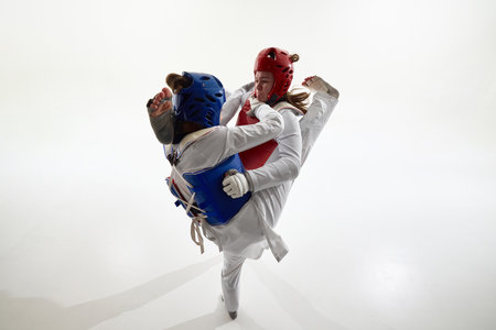 Blue and red taekwondo female athletes clashing in synchronized high kicks during dramatic studio fight.の写真素材