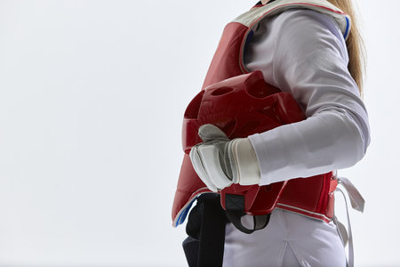 Cropped image of female taekwondo fighter standing in red protective gear, holding helmet isolated...