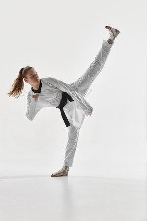 Young woman, taekwondo athlete performing high kick in studio showcasing strength balance and flexibility.の写真素材