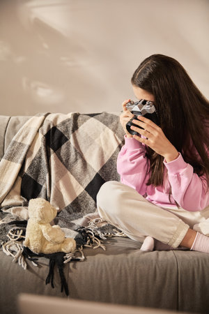 Teen girl taking photo of teddy bear toy with vintage camera on couch while practicing photo framing...