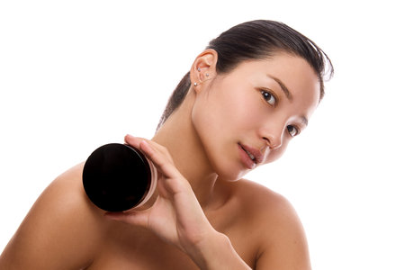 Confident young woman with flawless skin holding round cosmetic jar against white background.の写真素材