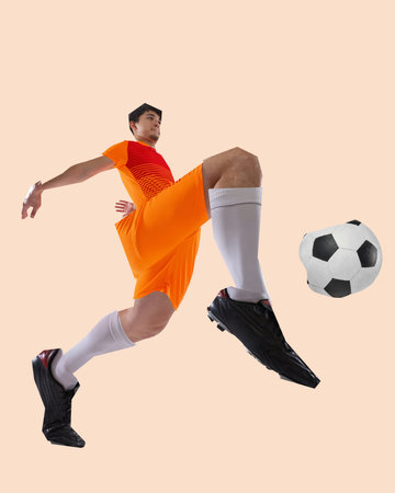 Dynamic male soccer player in orange uniform jumping forward toward ball with explosive energy over beige background. Cut out style.の写真素材