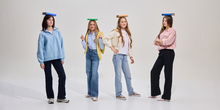 Four students stand in line with books on heads, expressing different emotions through posture and...