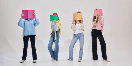 Group of students pose with colorful books covering faces, standing casually in modern classroom on...