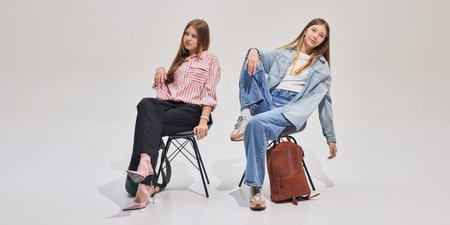 Two stylish students sitting on chairs with backpacks, relaxed and confident, ready for new school day or study session.の写真素材