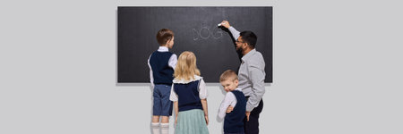 Teacher writes word dog on chalkboard while young schoolchildren in uniform stand close and observe attentively. Literacy lesson.の写真素材