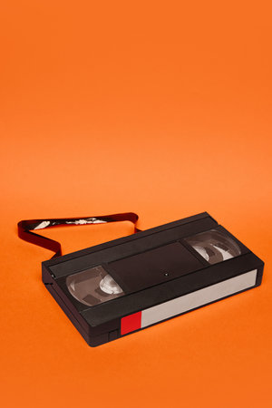VHS cassette with part of tape unraveled on orange background. Decay of analog memory. Concept of retro aestheticsの写真素材