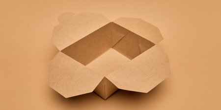 Open cardboard food box with flaps unfolded against light brown background. Sustainable takeaway...