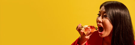 Excited young woman in red opens mouth wide to bite tomato pizza slice against bright yellow...