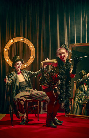 Cabaret couple posing in comic flirty motion with feather boa and canes in moody stage lighting.