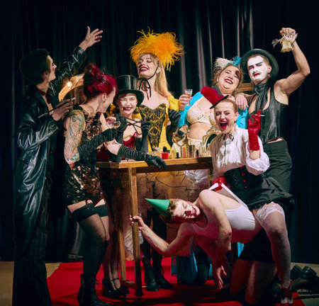 Cabaret cast celebrating around table with drinks and wild facial expressions in joyous vintage chaos.の写真素材