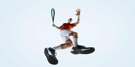 Bottom view of man, athlete jumps high with racket raised for strike wearing red shirt and white...