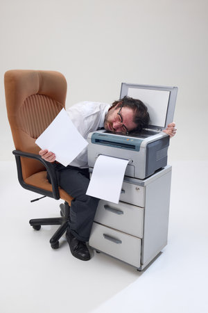 Man in shirt and tie lies over printer, holding paper, showing professional burnout, fatigue and...