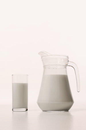 Milk in transparent glass stands beside matching pitcher in simple studio setup.の写真素材