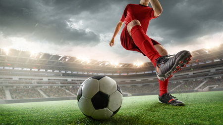 Cropped image of soccer player in red uniform during intense outdoor game, kicking ball against stormy sky. 3D render of stadium.の写真素材