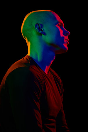 Side view portrait of handsome young guy with muscular body posing with serious and confident face on dark background in neon light.の写真素材