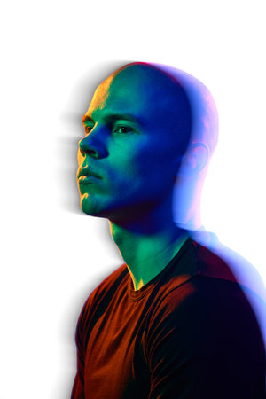 Portrait of handsome serious bald man with focused face posing against white background in multicolored neon light. Motion blur effect.の写真素材