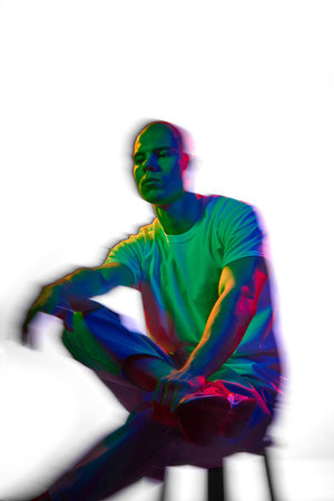 Portrait of attractive and serious bald young man in white t-shirt posing against white background with multicolored neon lighting with motion blur effectの写真素材