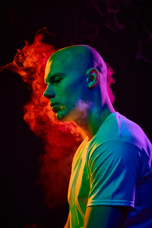 Side view portrait of handsome bald man in his 20s, looking to left with thoughtful expression on dark backgroundの写真素材