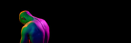 Back view of young, bald, muscular man, posing shirtless, looking downwards on dark background in multi-colored neon lightの写真素材