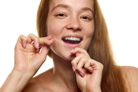 Close-up young, beautiful, redhaired woman with well-kept skin, flossing her teeth over white background.の写真素材