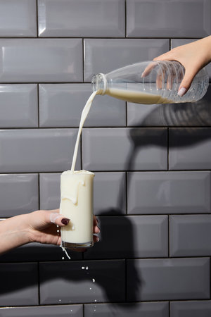 Hands hold plastic bottle and glass and pouring milk against brick grey wall.の写真素材