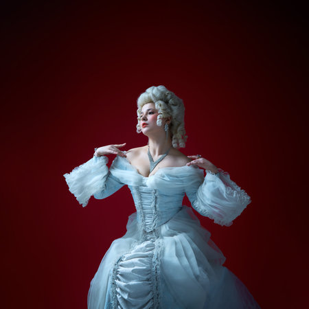 Vintage portrait of young graceful woman in image of medieval royal person in renaissance style dress on deep red background.の写真素材