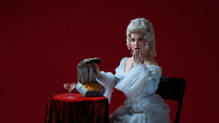 Hidden treasure. Female character in historical rococo look discovering snacks in fancy chest, surprised expression.の写真素材