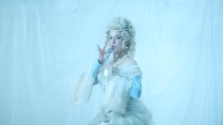 Elegant young woman as medieval royal person sipping milk with straw against light blue background.の写真素材