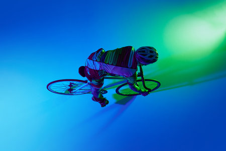 Top view of professional male cyclist in motion, training against blue studio background with green neon light.の写真素材