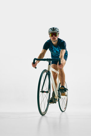 Full-length front view image of young man in full gear, cyclist in helmet and goggle riding bicycle isolated on white background.の写真素材