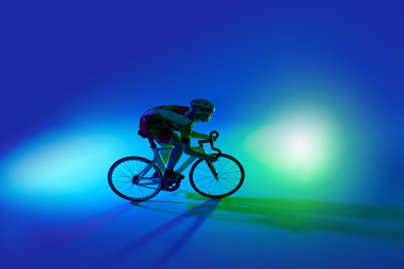 Top view of man, professional cyclist in motion, riding bicycle, training against blue background with green neon lightの写真素材