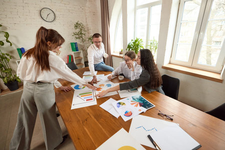 Business team analyzes charts and documents at wooden table in modern office, discussing data with focus.の写真素材