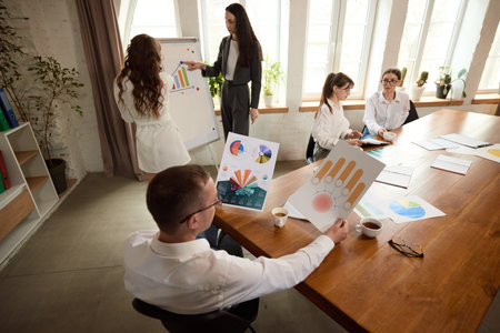 Business team discusses charts during presentation near whiteboard in bright office, reviewing visual data.の写真素材