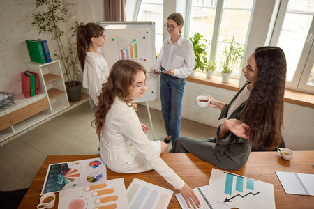 Business team reviews charts and documents with colleague presenting on whiteboard in bright office, discussing performance.の写真素材