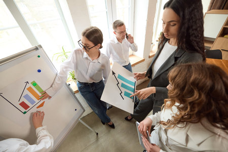 Business team discusses charts and data near whiteboard in modern office, pointing at visual aids.の写真素材