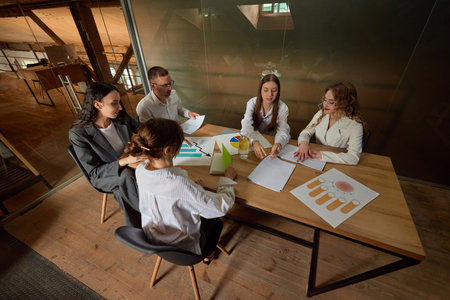 Business professionals review charts and documents, shares ideas, sits at large table. Concept of meeting, analysis, strategy, teamwork, collaboration.の写真素材