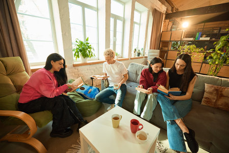 Group of young people sit with books and tea in loft living room enjoying literature and warm atmosphere.の写真素材
