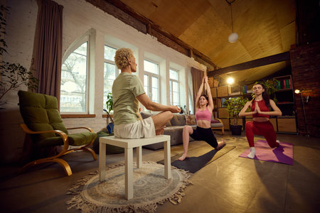 Group of friends practicing yoga together in spacious, bright room, stretching, meditating.の写真素材