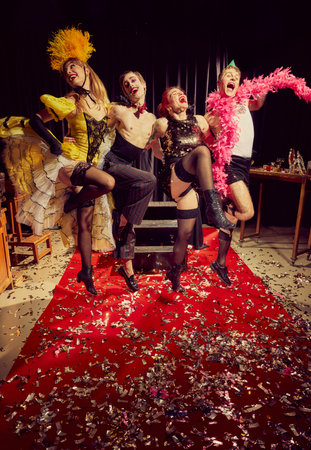 Four energetic cabaret performers posing on red carpet covered in confetti, joyful, theatrical expressions in their vintage attire.の写真素材