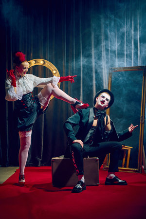 Cabaret woman raising leg toward seated man in dramatic pose with red gloves corset suitcase smoky lightsの写真素材