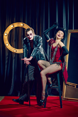 Cabaret duo performs dramatic pose with cane and stool wearing top hat gloves vintage makeup spotlight.の写真素材