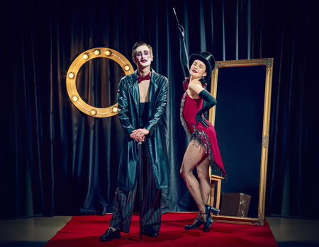 Stylized cabaret couple poses under lights wearing theatrical clothes cane hat and dramatic expressions.の写真素材