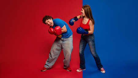 Playful young man and woman, couple wearing boxing gloves and acting out getting hit during a mock fightの写真素材