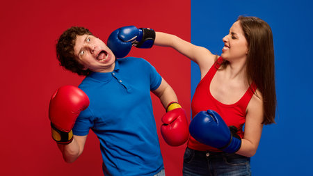 Dramatic young man and woman, couple wearing boxing gloves and acting out a punch to the face, with exaggerated expressionsの写真素材