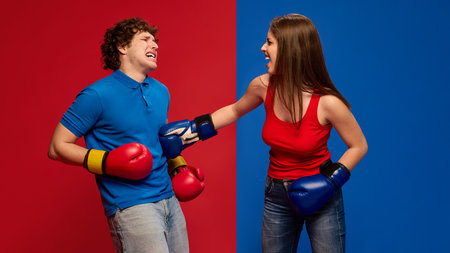Playful young man and woman, couple wearing boxing gloves and acting out getting hit in stomach, with exaggerated expressionsの写真素材