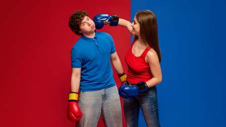 Humorous young man and woman, couple wearing boxing gloves and acting out punch to head, with exaggerated expressionsの写真素材