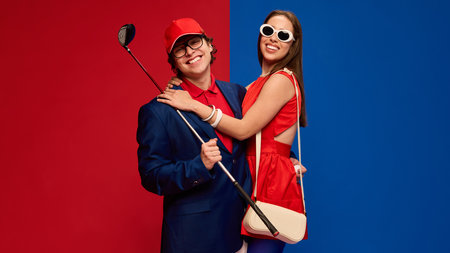 Happy couple hugging, smiling with golf club in hand, wearing colorful stylish outfits on red blue background.の写真素材