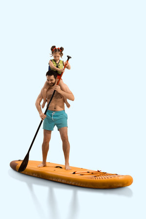 Smiling man, father standing on board, paddling with his daughter sitting on shoulders and holding paddle on sup board.の写真素材